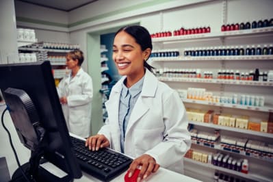 Cheerful young female pharmacist wearing labcoat working on computer