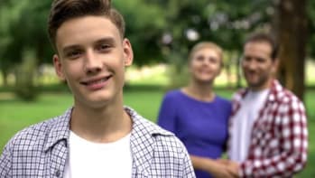 Teenage boy smiling on background of cheerful hugging parents, supporting family