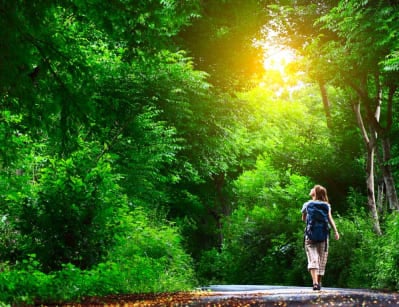 Young woman walking on green asphalt road in forest