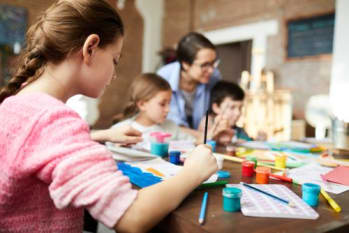 Back view portrait of teenage girl painting picture in art class with group of children