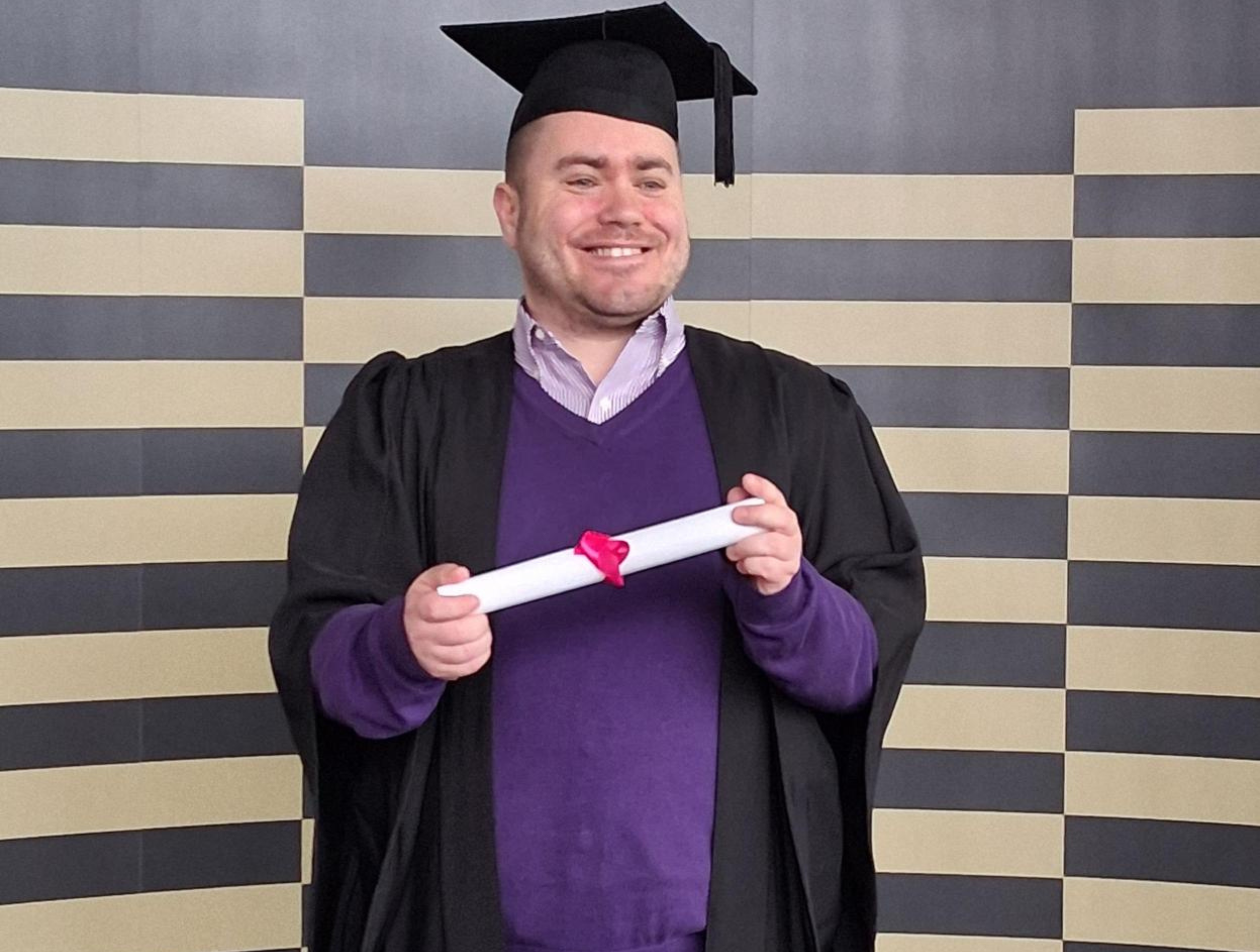 David Mc Mahon wearing a graduation gown and mortarboard cap, smiling at his graduation ceremony after completing a Preparation for Employment course at the Technological University of the Shannon.